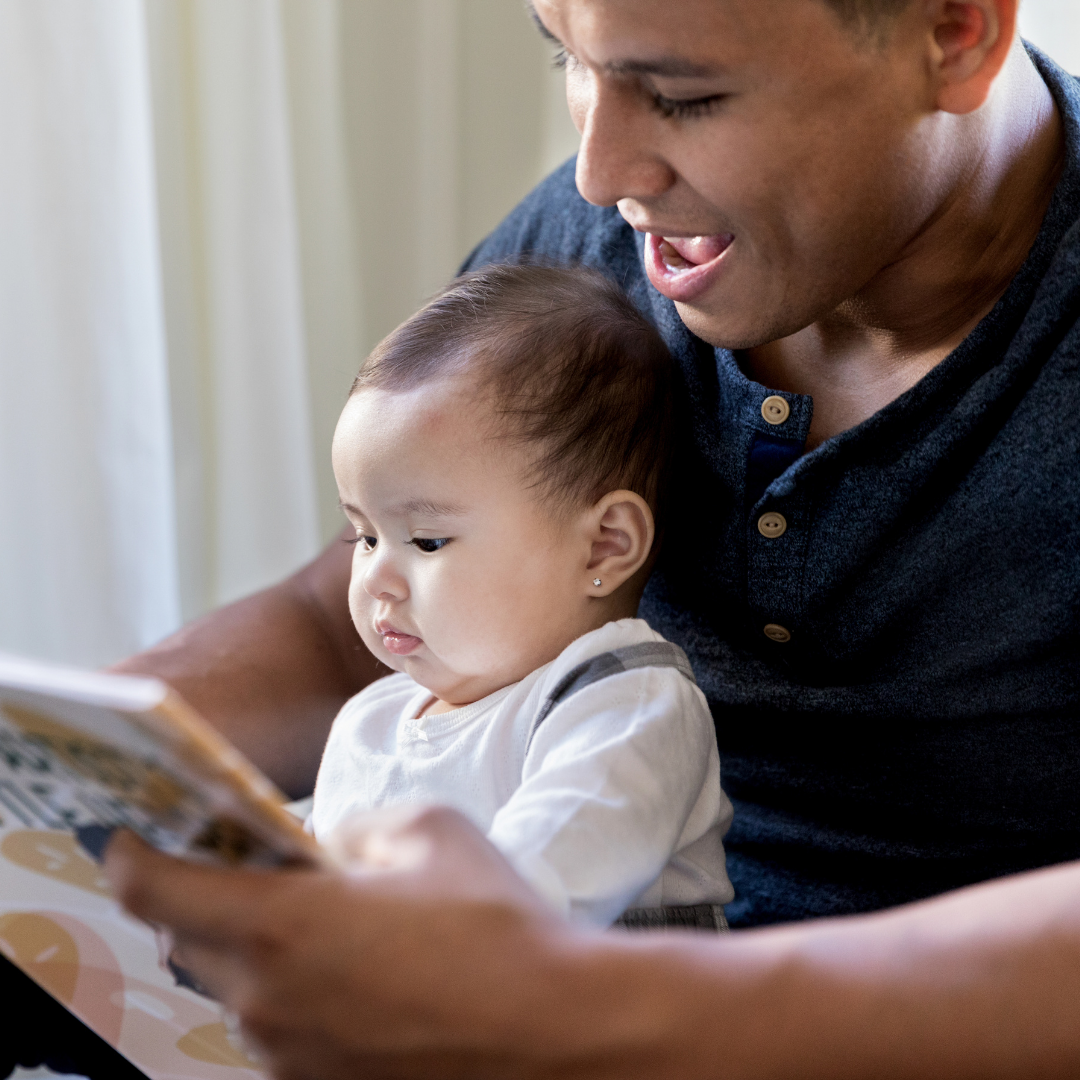 Smiling father reads picture book aloud to baby