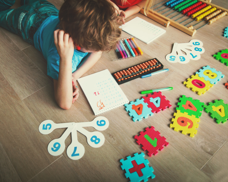 Image shows a toddler laying on the floor with various math tools surrounding him.