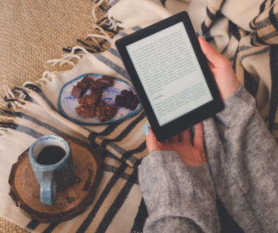 hands hold an ebook with a fall blanket, mug, and chocolates