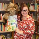Meridian Library staff member stands in front of bookshelves with book and puppet