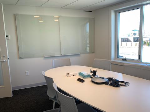 conference room with table and chairs, conferencing equipment, glass white board and windows overlooking street