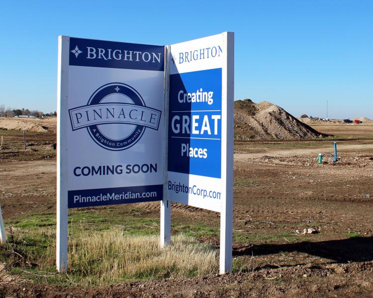 Sign says "Brighton Pinnacle Coming Soon" with dirt lot in the background
