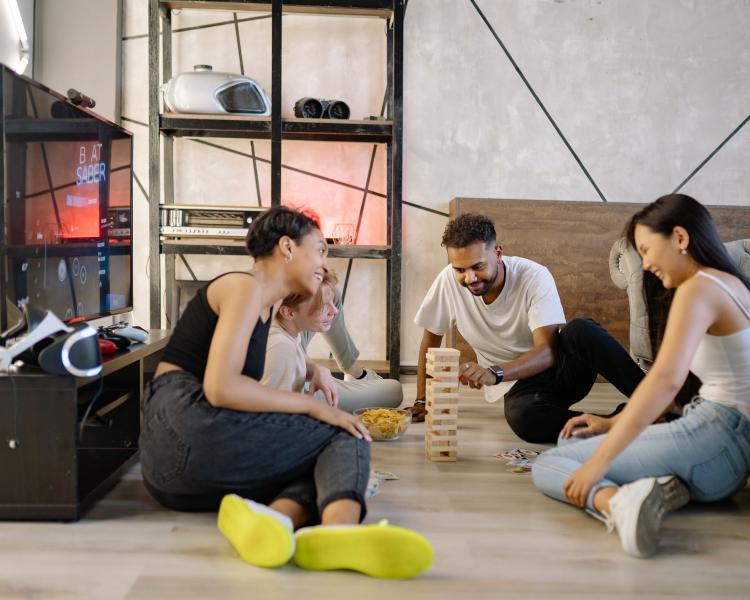 A group of four people sitting on the floor playing block building game, Jenga.