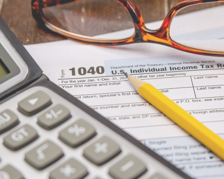 Tax form, calculator, pencil, and eyeglasses on a table.