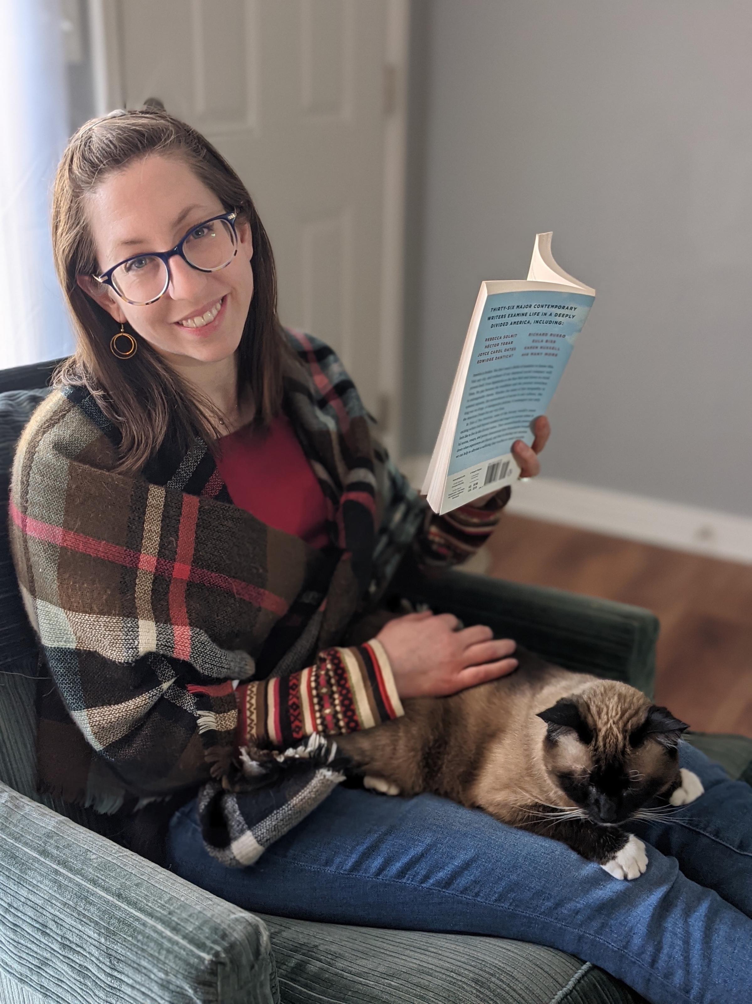 Emily sits in a chair reading a book, with a cat in her lap.